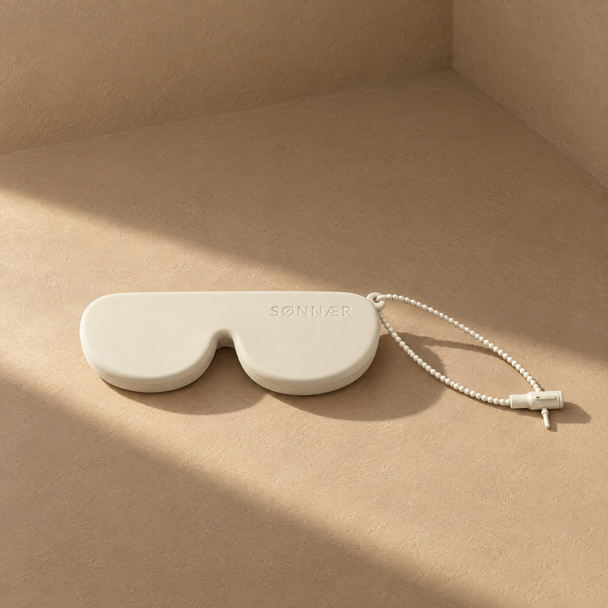 Cream SØNNÆR silicone sunglasses case in a sunlit plaster corner
