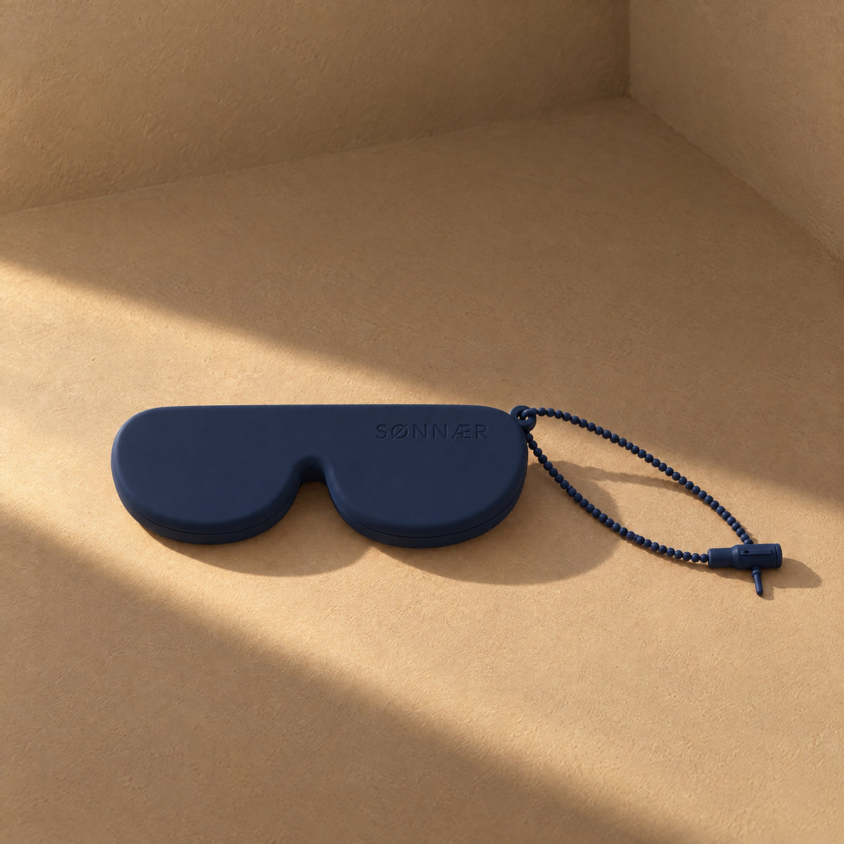 Navy SØNNÆR silicone sunglasses case in a sunlit plaster corner