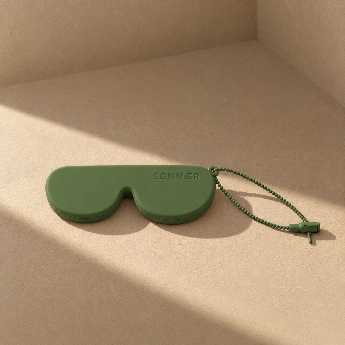 Olive SØNNÆR silicone sunglasses case in a sunlit plaster corner