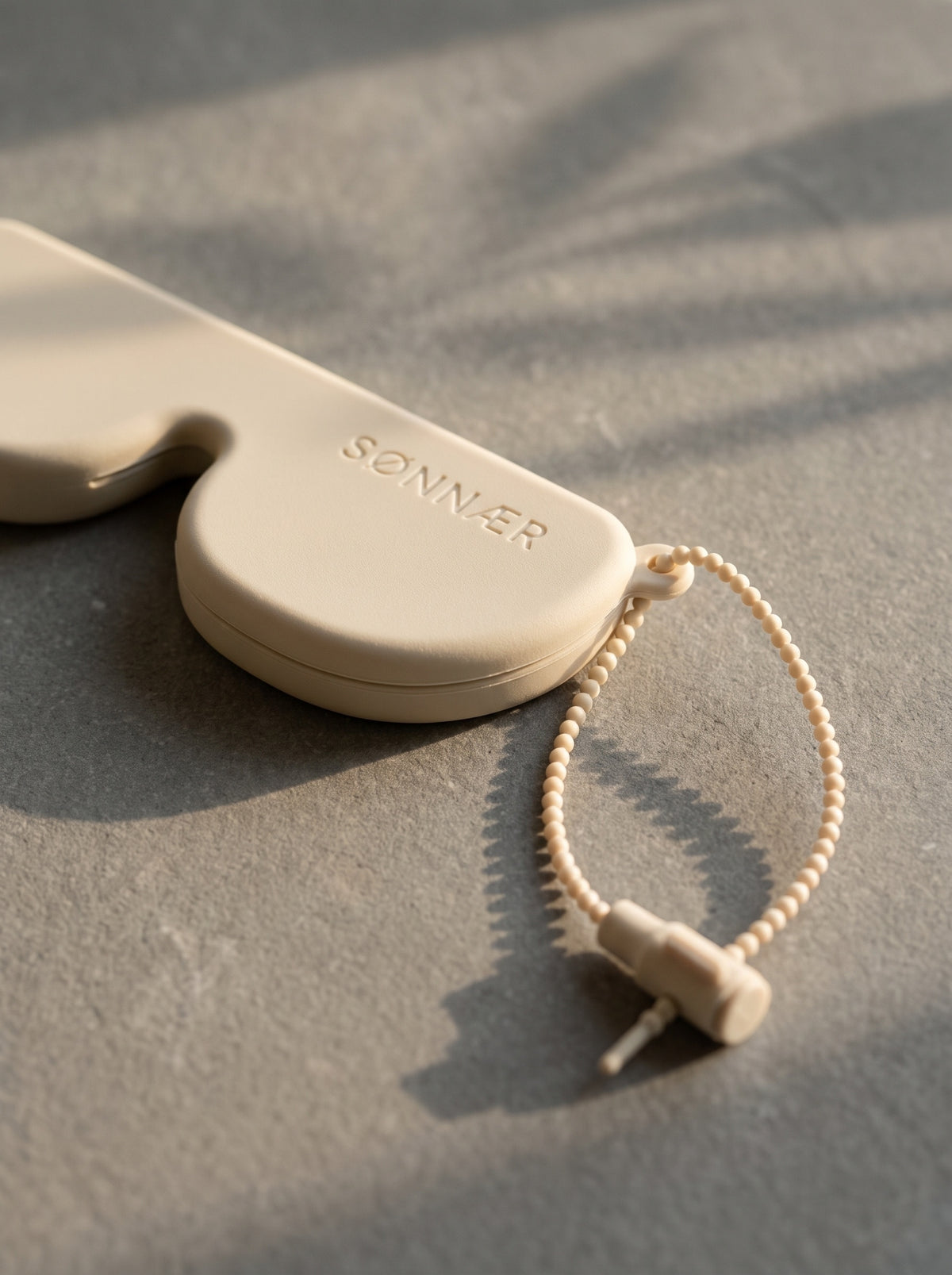 Close-up of the cream ball-chain lanyard and barrel clip on the SØNNÆR case