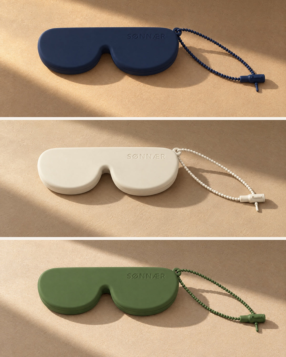 Three SØNNÆR silicone glasses cases in navy, cream and olive, each with its beaded lanyard, in the same sunlit plaster corner