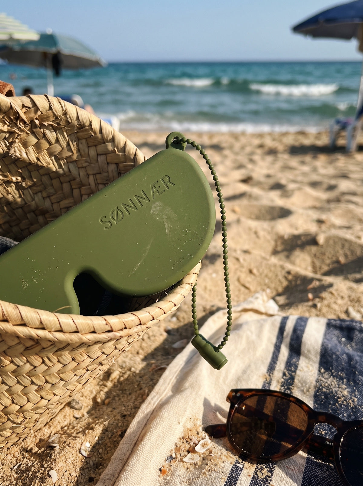 Olive SØNNÆR case in a straw beach bag on the sand