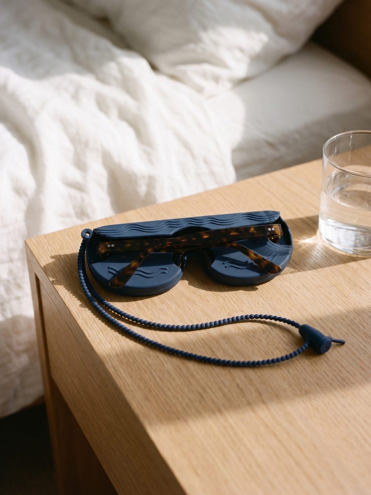 Navy SØNNÆR silicone case holding a pair of sunglasses on a nightstand